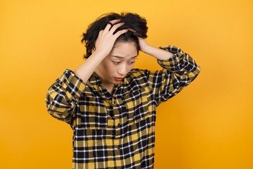 Young beautiful Asian woman wearing plaid shirt over yellow background suffering from strong headache desperate and stressed because of overwork. Depression and pain concept.