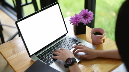 Cropped image of the hand is using a mockup computer laptop at the wooden working desk.