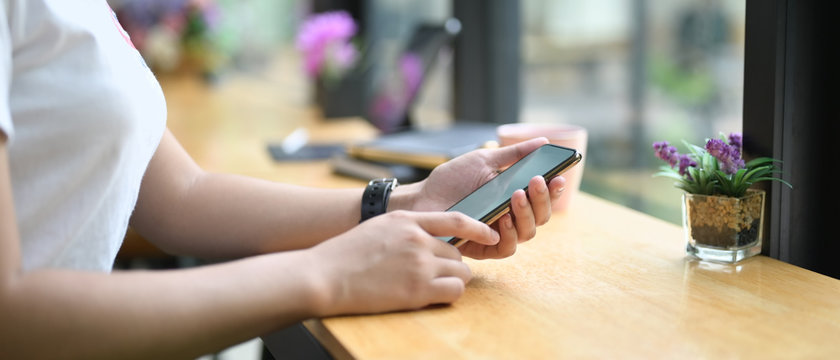 Cropped image of a woman is using a smartphone while sitting at the wooden counter bar.
