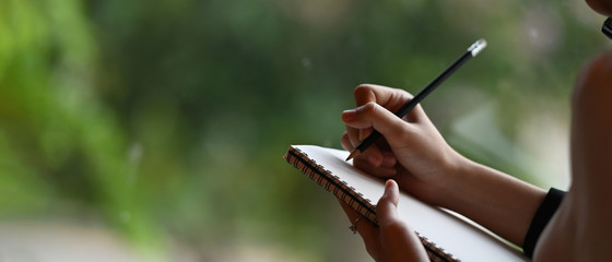 Cropped image of a businesswoman's hand is taking notes while standing over the office glass wall.