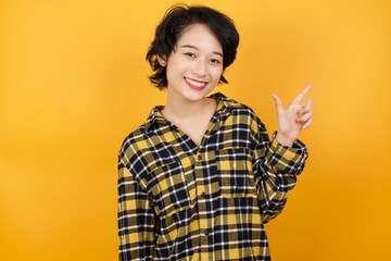 Young asian woman with short hair wearing plaid shirt standing over yellow background pointing up with fingers number eight in Chinese sign language BÄ.