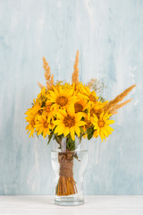 A bouquet of yellow flowers, sunflowers, in a glass vase on a blue background. Copy space.