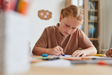 Portrait of freckled red haired girl drawing pictures with crayons while enjoying art class in school or development center, copy space