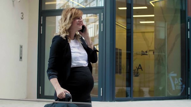 A pregnant business woman talking on her mobile phone while exiting the building