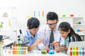 Young Asian boy and girl smile and having fun while doing science experiment in laboratory classroom with Teacher. Study with scientific equipment and tubes. Education concept.