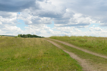Summer landscape with a view of a dirt road through a field and hills
