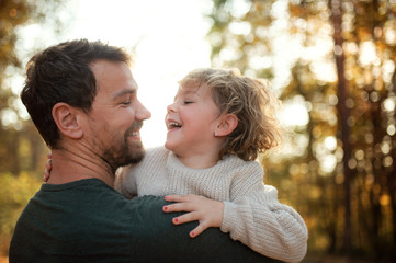 Mature father holding small daughter on a walk in autumn forest.