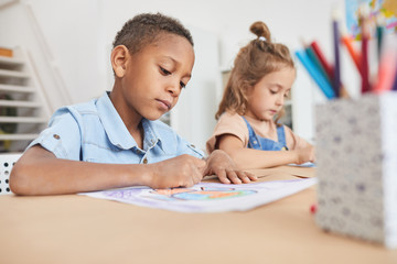 Portrait of cute African-American boy coloring pictures with crayons while enjoying art and craft...