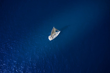 White sailboat in the rays of the sun on blue water top view