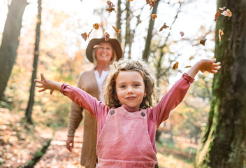 Small girl with grandmother on a walk in autumn forest, having fun.