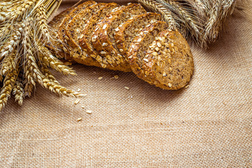 Obraz premium Loaf bread. Rye bakery with crusty loaves and crumbs. Fresh loaf of rustic traditional bread with wheat grain ear or spike plant on natural cotton background. Bio ingredients, very healthy seeds.
