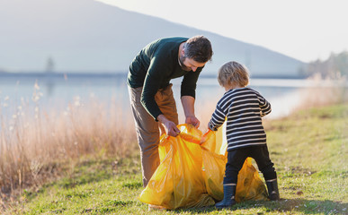 Father with small son collecting rubbish outdoors in nature, plogging concept.