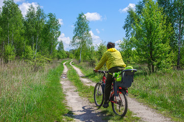 Fototapeta na wymiar Dad in bright clothes rides his little daughter in a bicycle seat on a bicycle along a dirt road through the woods