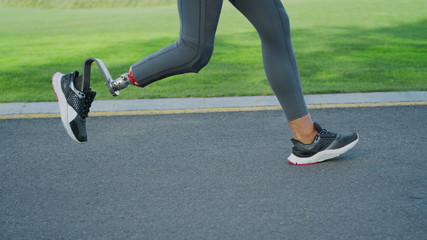 Fototapeta na wymiar Woman with prosthetic leg running on road. Female sportsperson training outdoors