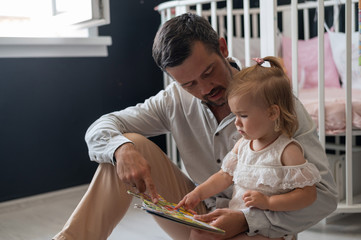 Obraz premium A caring father reads a fairy tale to his little daughter in the children's bedroom.
