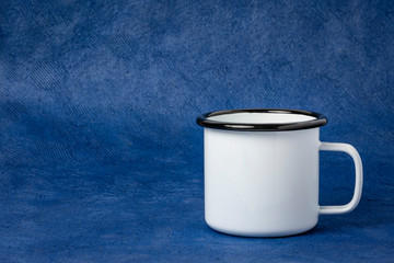 white metal enamel cup of tea on a blue textured paper background with a copy space