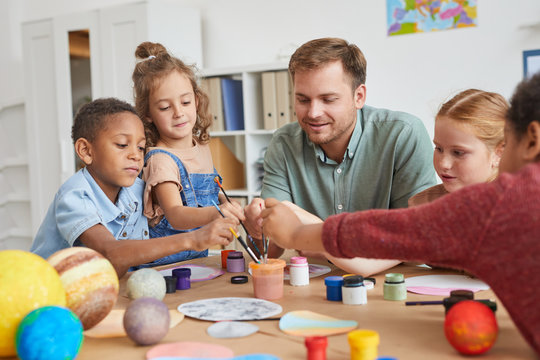 Portrait of multi-ethnic group of children holding brushes and painting planet model while enjoying art and craft lesson in school or development center, copy space