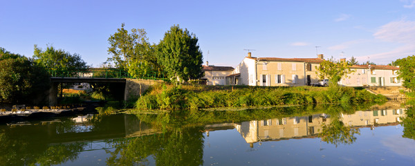 Fototapeta na wymiar Panoramique de barques et reflets des maisons sur la Sèvre Niortaise à Damvix (85420), Vendée en Pays de la Loire, France
