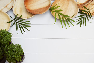 Fototapeta na wymiar Platos de bambú con plantas de hojas verdes sobre fondo de tablas blancas vistas desde arriba.