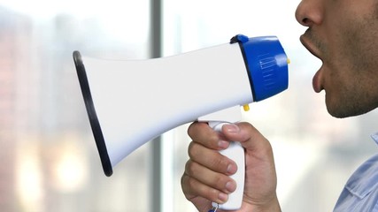 Close up man talking into megaphone. Abstract blurred background. Warning or announcement concept.