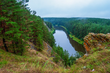Fototapeta na wymiar Beautiful river landscape with forest slopes of mountains. Limestone rocks in the Ural mountains. Cloudy sky in the background.