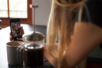 Young woman taking a selfie leaning on kitchen table with coffee