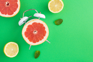 Half a grapefruit on the dial of the alarm clock and sliced fresh fruits on the green surface