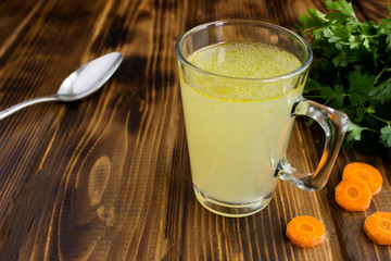 Chicken broth in the glass on the brown wooden surface