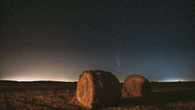 Comet Neowise C/2020 F3 In Night Starry Sky Above Haystacks In Summer Agricultural Field. Night Stars Above Rural Landscape With Hay Bales After Harvest. Agricultural Concept. 4K Timelapse