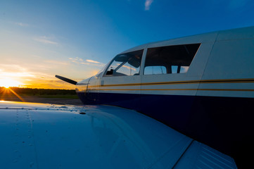 Close-up of a small parked plane with a propeller against the backdrop of a sunset.