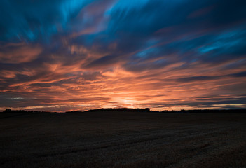 Plakat Langzeitbelichtung von einem Sonnenuntergang im Sommer auf einem geerntetem Getreidefeld