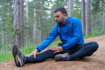 Young athlete in blue sports wear stretching in woods.