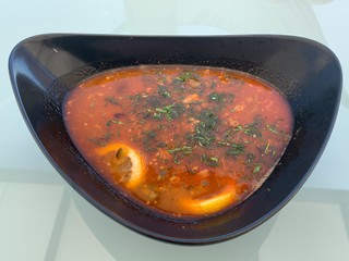 A plate of hodgepodge on a white table. First dish with meat and vegetables. Soup with herbs and lemon.