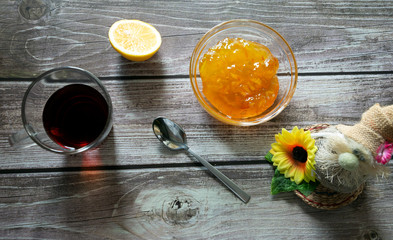 A cup of tea, orange jam, lemon and a toy on a dark wooden background.