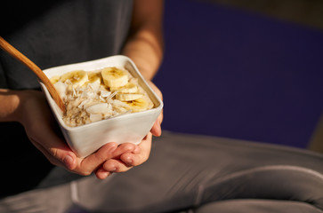 woman holding healthy breakfast bowl sitting on yoga mat after workout