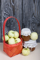Apples in a red wicker basket. Jam in jars and apples nearby. Fruit harvest.
