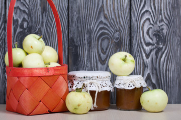 Apples in a red wicker basket. Jam in jars and apples nearby. Fruit harvest.