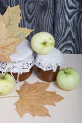 Apple jam in jars. Nearby are apples and dried maple leaves. Fruit harvest.