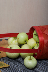 An overturned basket of apples. Nearby are apples and dried maple leaves. Fruit harvest.