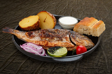 Grilled dorado with baked potatoes, matnakash and red sauce. Served in a cast iron pan