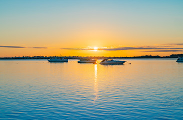 Three boats moored near horizon at sunrise over blue water of Tauranga harbour with intense golden glow on horizon.