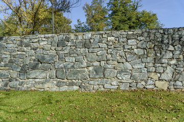 Green grass lawn with wall decorative uneven cracked real stone surface