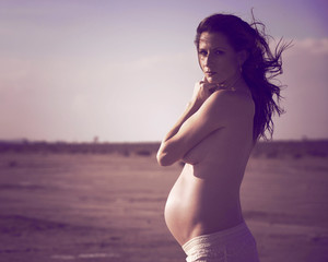 A topless pregnant woman in a white dess in the desert