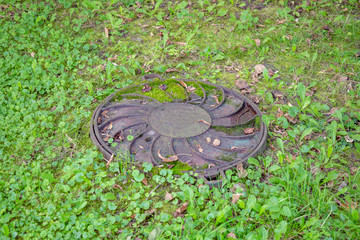 Old round manhole among lush green grass