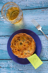 A quiche on a blue rustic table with a jar of beer and a loving note on a sticker