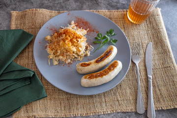 A plate with two sausages and sauerkraut with a drink and cutlery