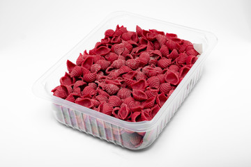 Raw colored conchiglie pasta in a plastic box isolated on a white background