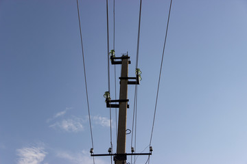 Electric transmission lines, pole with insulators and wires against the blue sky
