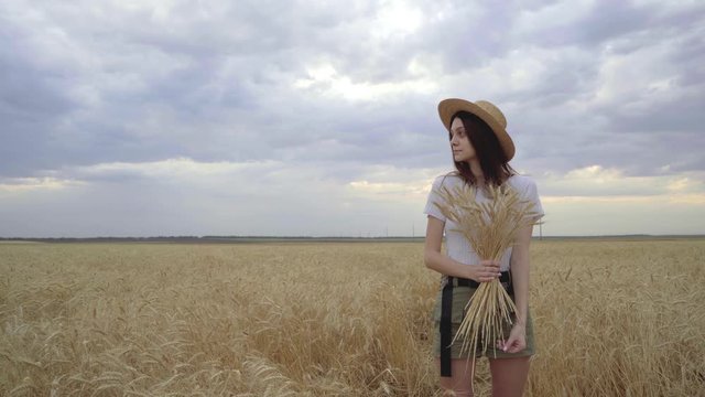 Young girl in a straw hat stands in a wheat field