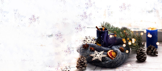 Obraz premium Blue cup with tea and candle on the background of window with winter pattern. The concept of Christmas decor. Cozy Hugge Style.